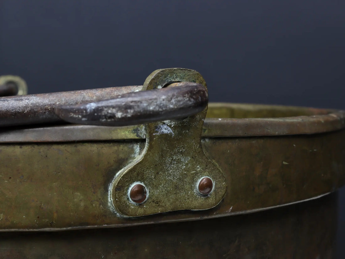 19th Century Dutch hand-hammered brass cauldron featuring a heavy-duty forged iron swing handle, authentic copper rivets, and a rolled rim detail.