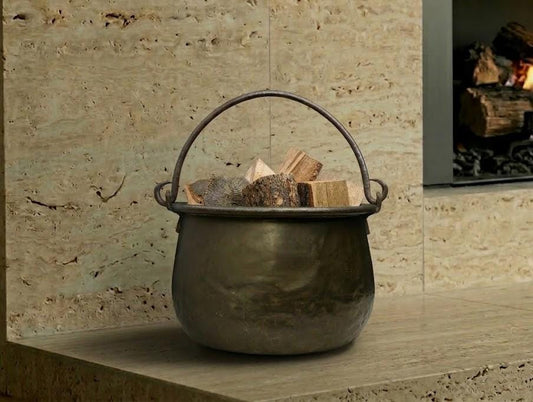 Antique brass kettle firewood holder on a stone hearth with logs, perfect for rustic fireplace decor and storage.